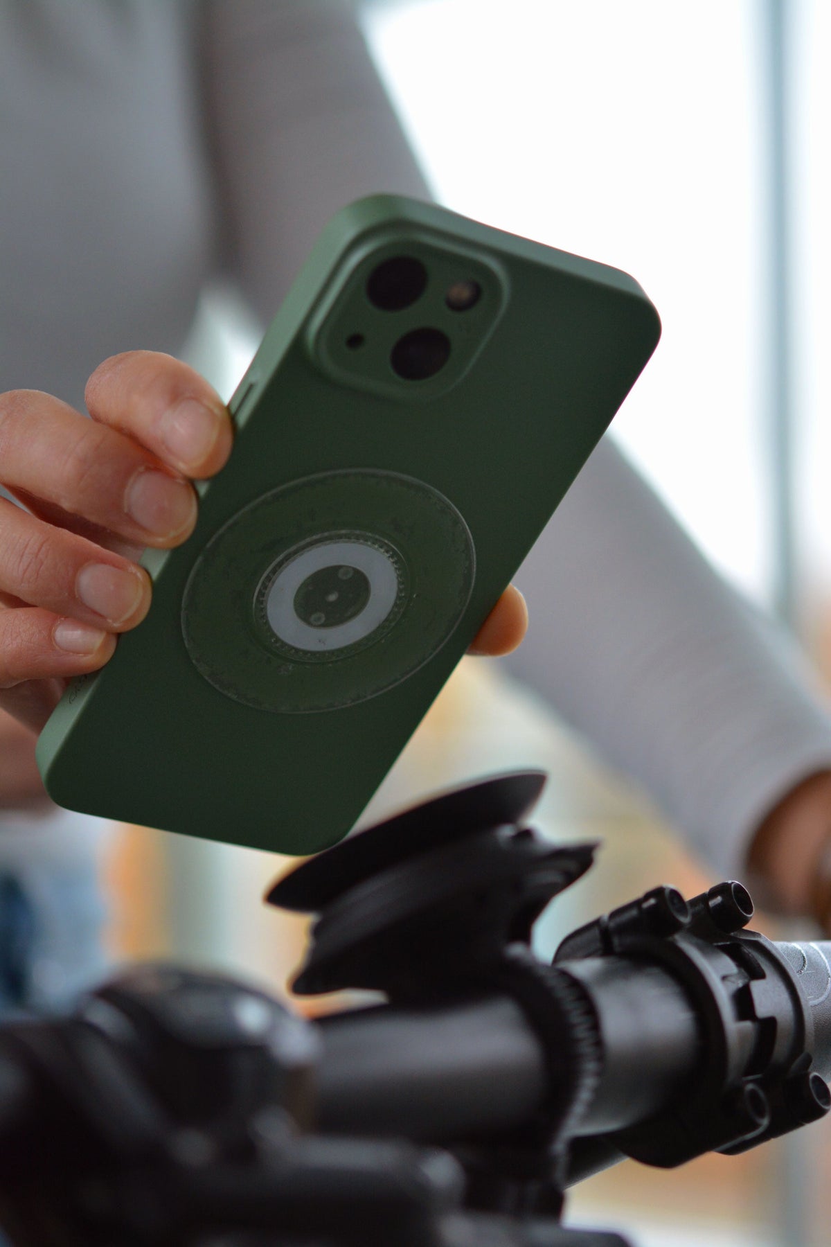 FIDLOCK VACUUM Klebepad für Smartphones, universell, transparent — transparentes Pad am Smartphone angebracht, vor einer VACUUM Halterung gezeigt